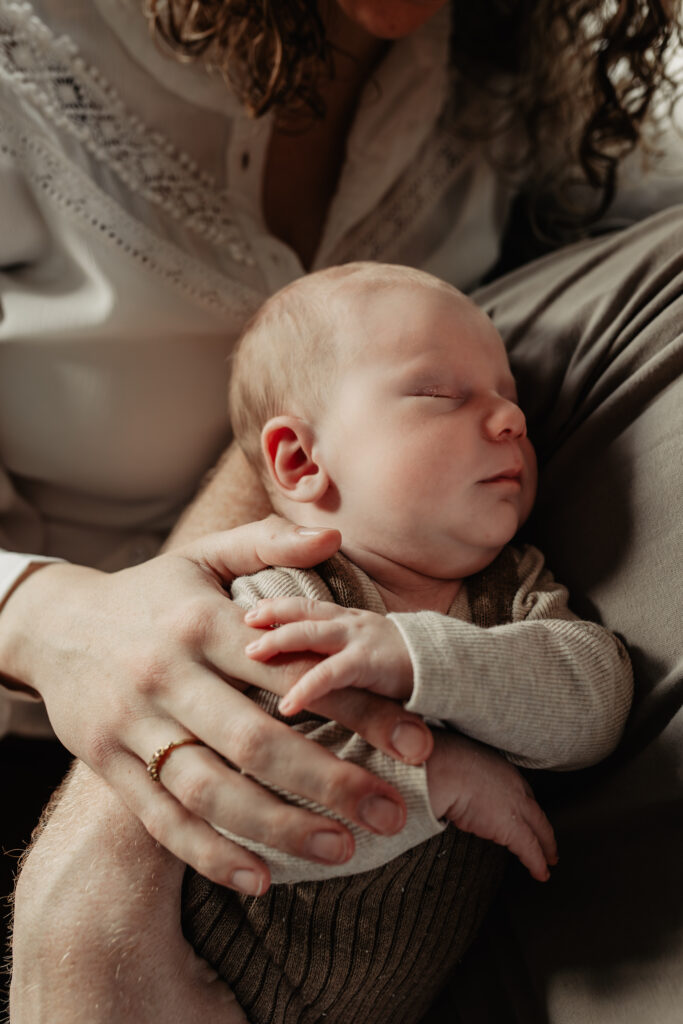Pasgeboren baby slapend tegen de borst van ouder tijdens newbornshoot aan huis, gefotografeerd met natuurlijk licht.