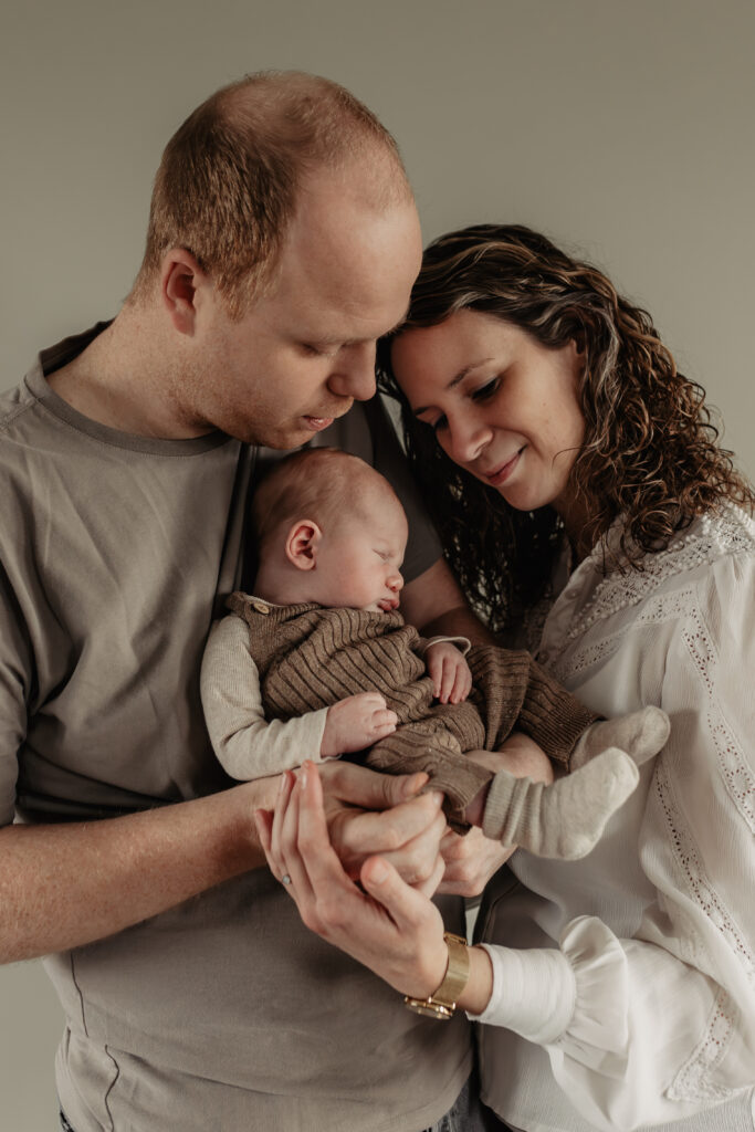 Ontspannen moment tijdens newbornshoot: ouders knuffelen met hun baby.
