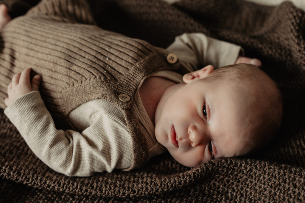 Detailfoto van een newborn slapend op een donkerbruin dekentje in zacht daglicht.