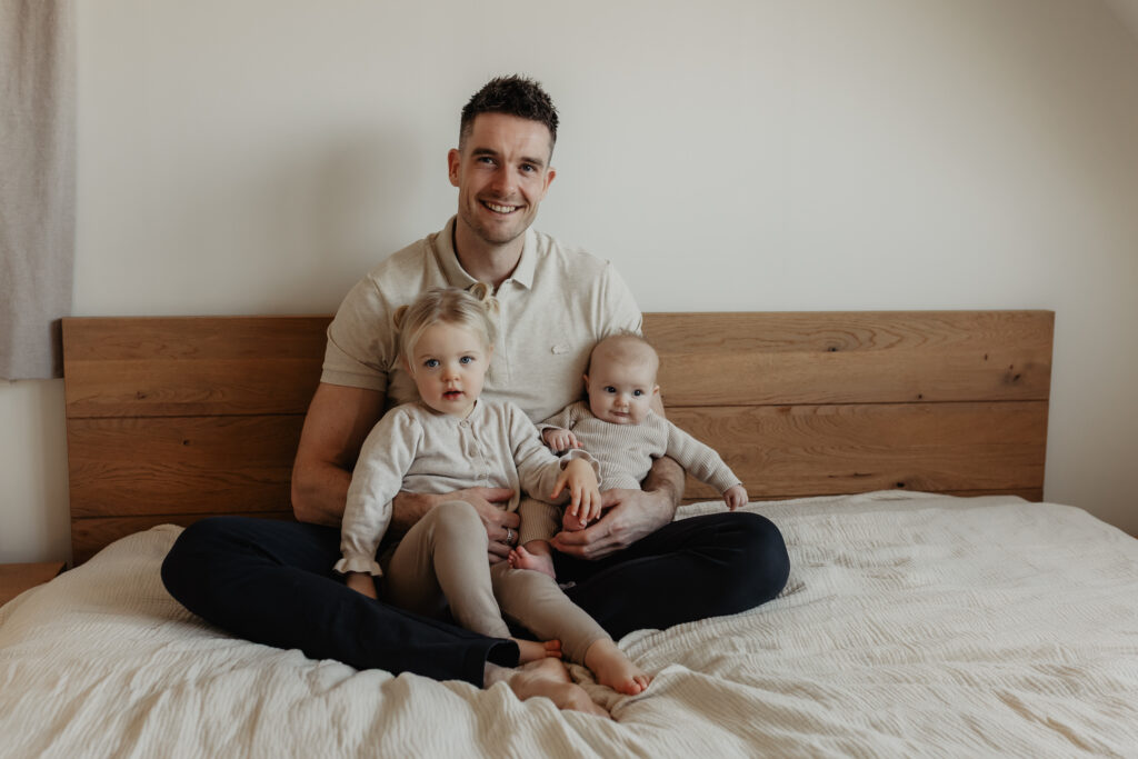 Vader, zus en newborn samen bij het raam tijdens newbornshoot aan huis in Baarle-Nassau