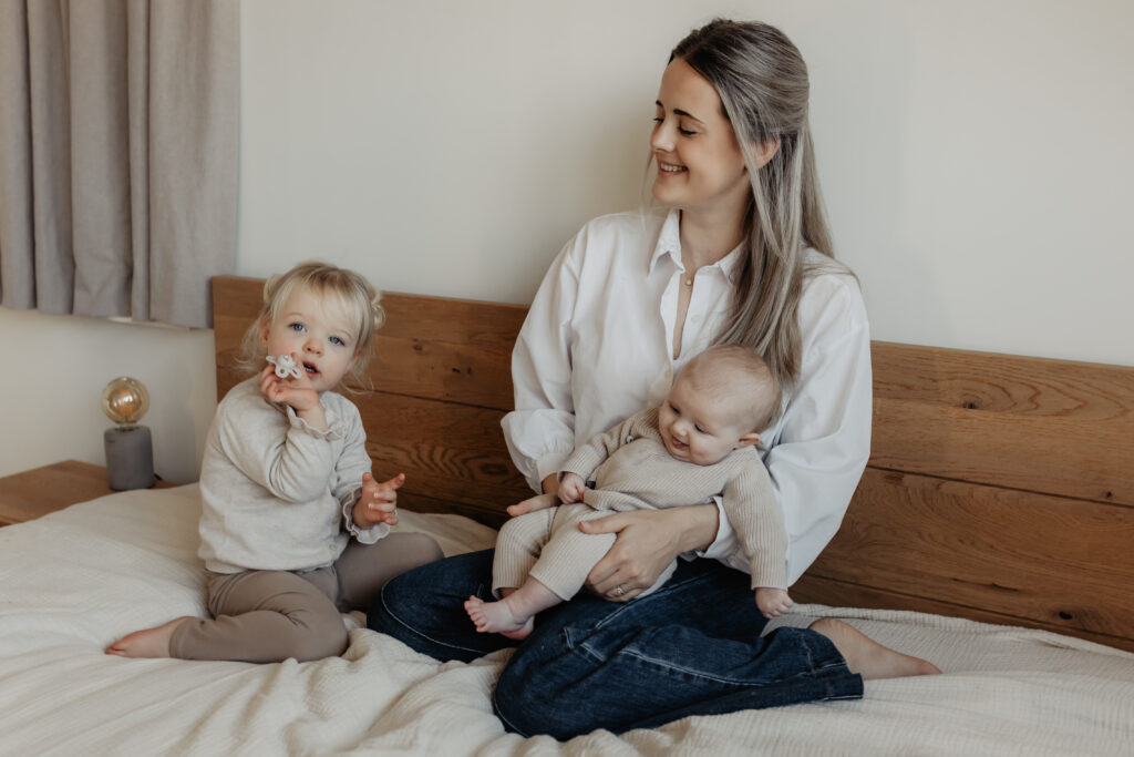 Grote zus houdt het speentje vast op bed tijdens newbornshoot aan huis Baarle-Nassau